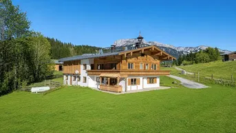 Traditionelles Holzhaus im alpenländischen Stil mit Bergblick und grüner Umgebung.