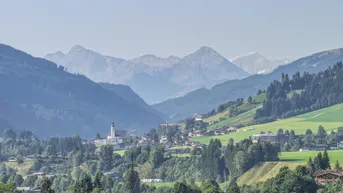Panoramablick auf ein malerisches Dorf in einem grünen Tal, umgeben von majestätischen Bergen.