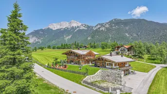 Großzügige Chalet-Anlage in alpiner Landschaft mit beeindruckendem Bergblick unter blauem Himmel.