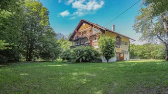 Traditionelles Haus mit mehreren Balkonen, umgeben von viel Grün und mit Bergblick.