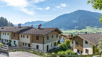 Traditionelle Häuser in alpiner Landschaft mit weitem Blick auf die Berge und grüne Täler.