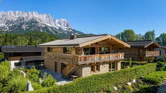Traditionelles Holzhaus mit Steinfassade und Bergblick in alpiner Umgebung.