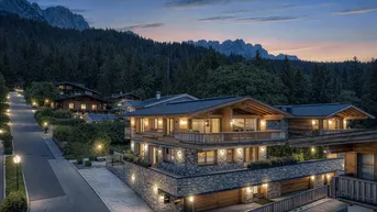 Luxuriöses Chalet in den Bergen bei Sonnenuntergang mit beleuchteter Zufahrt und alpiner Architektur.