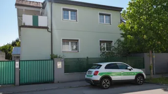 Vorderansicht des Hauses mit hellgrüner Fassade, Fenstern und einem gepflegten Vorgartenbereich.