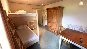 Gemütliches Schlafzimmer mit Etagenbett, Holzschrank und kleinem Esstisch für Gäste.