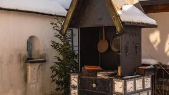 Traditioneller Außenofen im verschneiten Garten mit Bergblick und rustikalem Design.