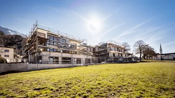 Neubauprojekt im Bau mit Gerüst, umgeben von grünen Wiesen und Bergen unter strahlendem Sonnenschein.