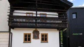 Traditionelles Gebäude mit Holzbalkon und weißer Fassade unter blauem Himmel.