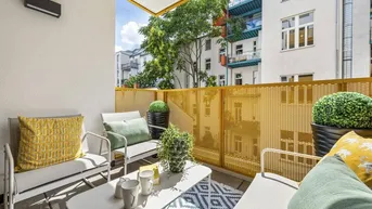 Gemütlicher Balkon mit gelbem Geländer, bequemen Sitzgelegenheiten und Blick ins Grüne.