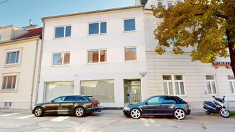 Vorderansicht des Gebäudes mit mehreren Fenstern und parkenden Autos auf der Straße.