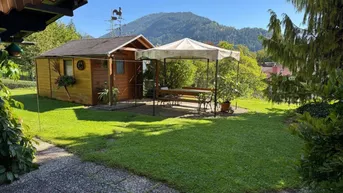 Blick von der überdachten Terrasse auf den Garten mit Pavillon und Bergblick.