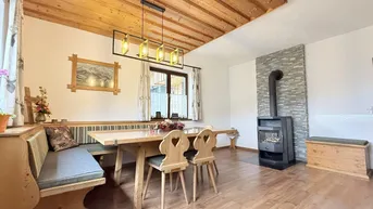 Gemütlicher Essbereich mit Holztisch, Eckbank und einem modernen Holzofen für behagliche Wärme.