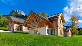 Traditionelle Holzhäuser in alpiner Landschaft mit Bergblick unter blauem Himmel.
