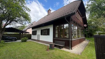 Hausansicht mit Carport und gepflegtem Gartenbereich, umgeben von Bäumen und Hecken.