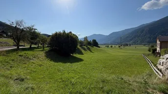 Weitläufige grüne Wiesen und Felder mit Blick auf die umliegende Berglandschaft unter strahlendem Sonnenschein.