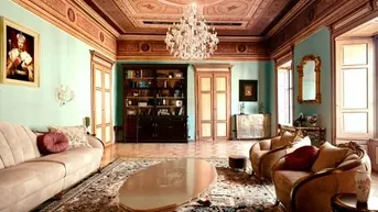 Prächtiges Wohnzimmer mit aufwendig verzierter Decke, Kronleuchter und luxuriösen Möbeln.