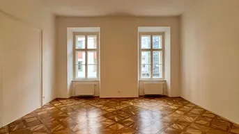 Helles Zimmer mit Fischgrätparkett und zwei Fenstern, das viel Tageslicht hereinlässt.