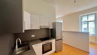 Kompakte Einbauküche mit modernen Geräten und integriertem Kühlschrank in hellem Raum.