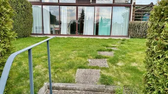 Grüner Gartenbereich mit Rasenfläche und Zugang zur verglasten Terrasse des Hauses.