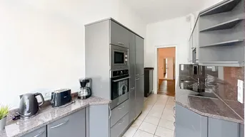 Funktionale Küche mit grauen Schränken, Granitarbeitsplatten und integrierten Geräten auf Fliesenboden.