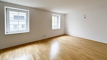Heller Wohnraum mit Parkettboden und zwei Fenstern, die viel Tageslicht hereinlassen.