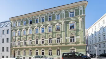 Historisches Eckgebäude mit grüner Fassade und reich verzierten Fenstern in städtischer Umgebung.