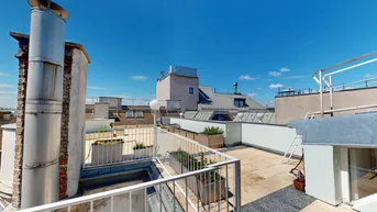 Weitläufige Dachterrasse mit Pflanzkübeln und Blick über die Dächer der Stadt an einem sonnigen Tag.