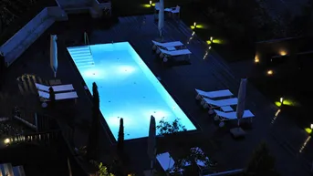 Beleuchteter Außenpoolbereich bei Nacht mit Holzdeck und Liegestühlen, ideal für entspannte Abende.