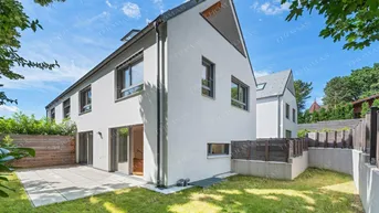 Modernes weißes Reihenhaus mit gepflegtem Garten und sonniger Terrasse unter blauem Himmel.