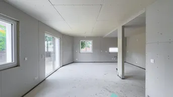 Unfertiger Wohnbereich im Rohbau mit großen Fenstern und Zugang zum Garten.