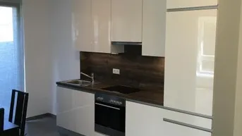 Moderne Küche mit weißen Hochglanzfronten, integrierten Geräten und Fliesenboden.