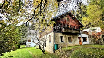 Charmantes Landhaus mit Holzbalkonen und Steinfassade, umgeben von Herbstbäumen.