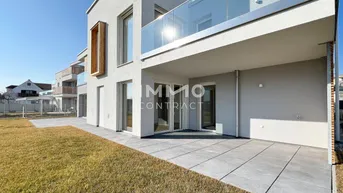 Moderne Wohnanlage mit großer Terrasse, Rasenfläche und Balkonen unter blauem Himmel.