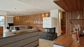 Moderner offener Wohnbereich mit integrierter Küche, Kamin und Holzwänden.
