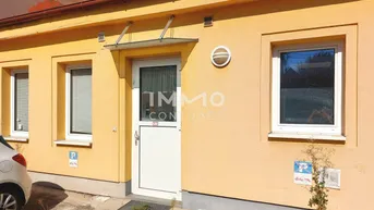 Gelbe Fassade eines Gebäudes mit Eingangstür und Fenstern, sowie einem kleinen Kiesbereich davor.