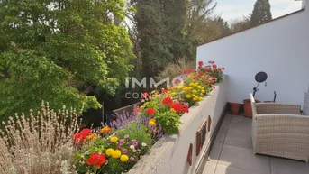 Sonniger Terrassenbereich mit bunten Blumenbeeten und Sitzgelegenheiten.