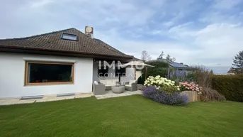 Großer gepflegter Garten mit Rasenfläche, Blumenbeeten und einer kleinen möblierten Terrasse am Haus.