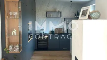 Offener Wohnbereich mit Kamin, Holzboden und Übergang zur modernen Küche.