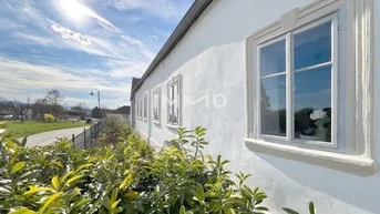 Weiße Fassade eines traditionellen Gebäudes mit Fenstern und umgebender Natur unter blauem Himmel.