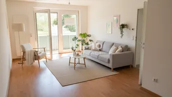 Helles Wohnzimmer mit Laminatboden, bequemer Couch und Zugang zum Balkon.