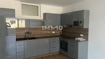 Moderne Küche mit grauen Hochglanzfronten, Holzakzenten und integrierten Geräten.