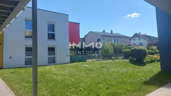 Blick auf das Gebäude mit einer großen Rasenfläche im Vordergrund und weiteren Häusern im Hintergrund.