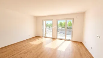 Helles, leeres Zimmer mit Holzboden und Zugang zu einem Balkon oder einer Terrasse.