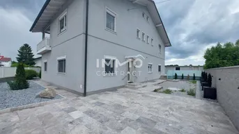 Graues Einfamilienhaus mit gepflastertem Vorplatz und modernem Design unter bewölktem Himmel.