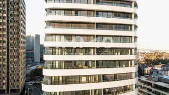 Moderne Hochhausfassade mit geschwungenen Balkonen und großen Fenstern in urbaner Umgebung.