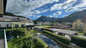 Blick auf die Wohnanlage mit mehreren Gebäuden, einem Teich, Carports und der umliegenden Berglandschaft.