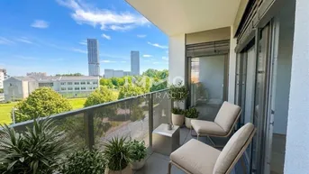Möblierter Balkon mit Stadtblick, Pflanzen und Sitzgelegenheiten unter blauem Himmel.