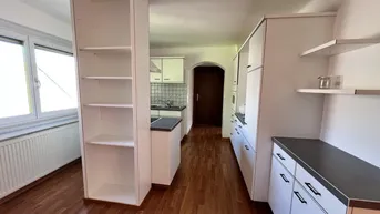 Funktionale Küche mit weißen Schränken, dunkler Arbeitsplatte und Laminatboden.