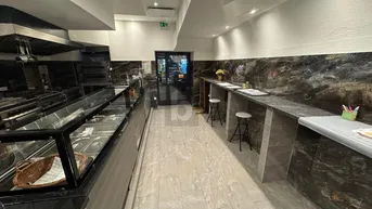 Blick in eine professionelle Gewerbeküche mit Theke, Sitzgelegenheiten und modernen Edelstahlgeräten.