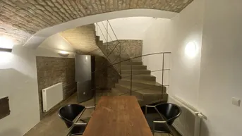 Gewölbekeller mit Backsteindecke, Steintreppe und einem Esstisch.